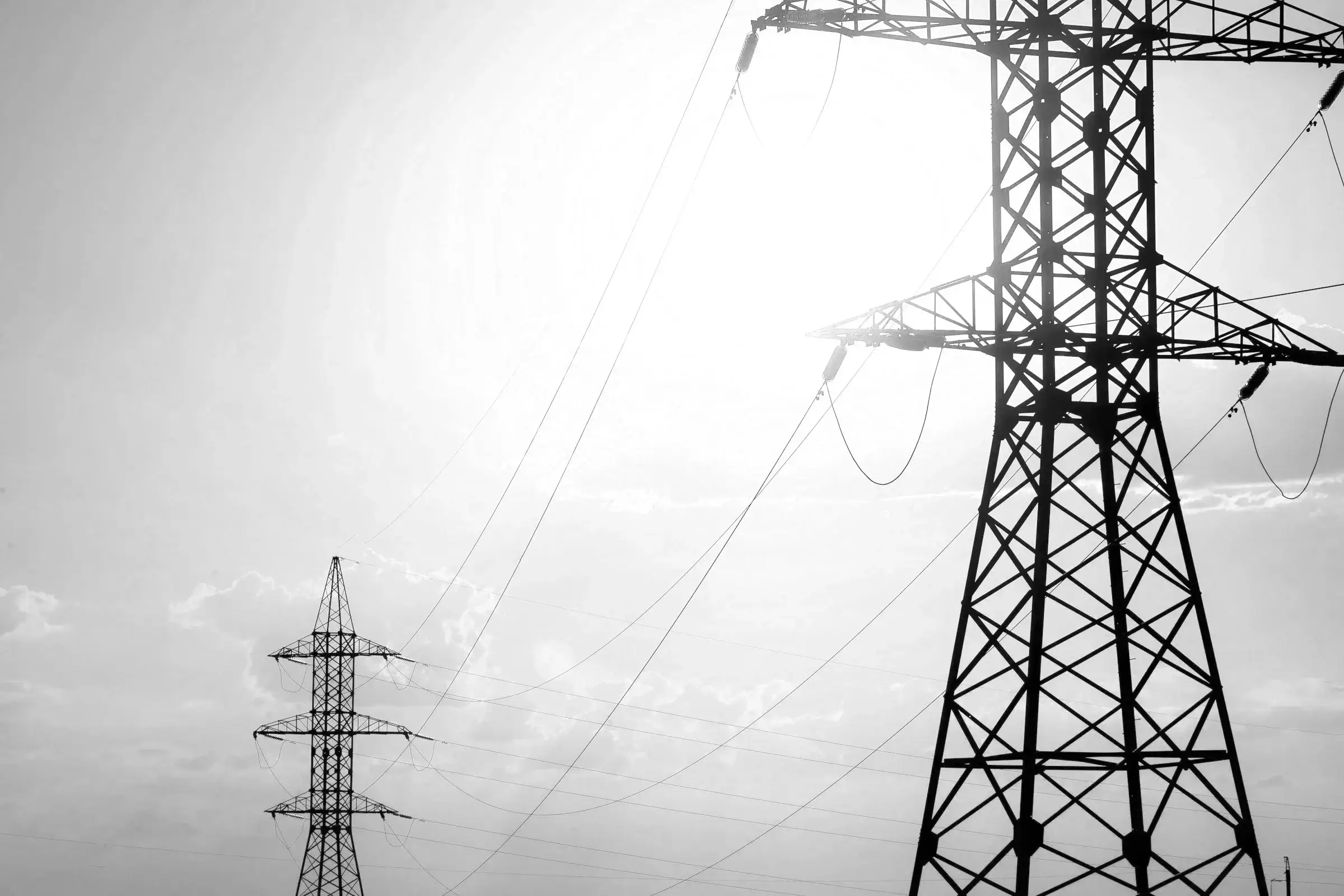 High-voltage transmission towers silhouetted against a bright sky